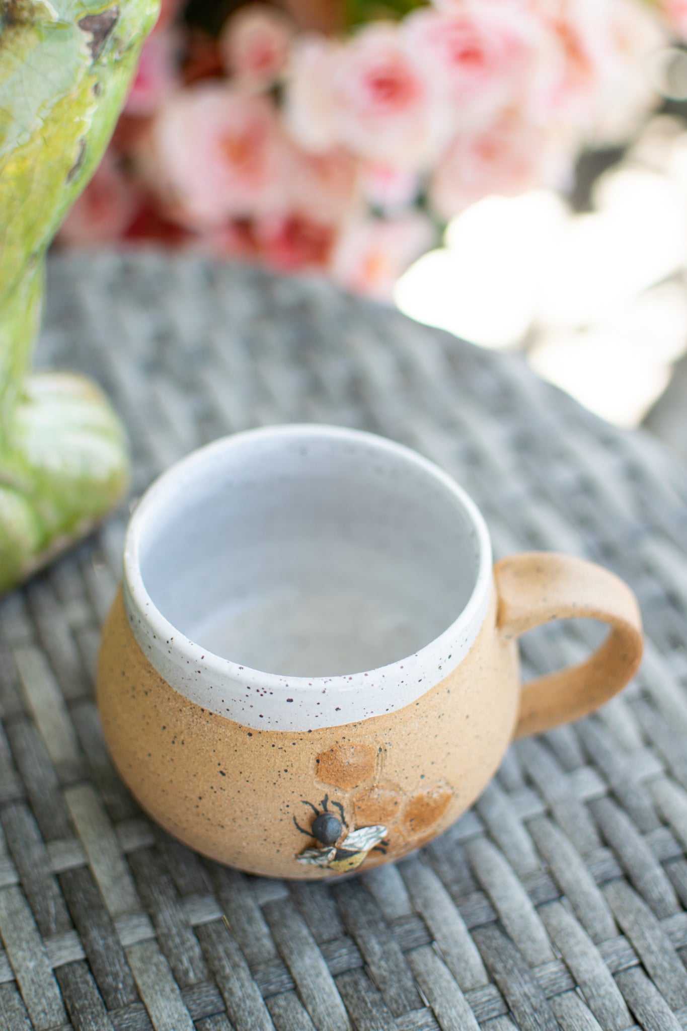Ceramic mug with speckled design on a textured surface with blurred flowers in the background