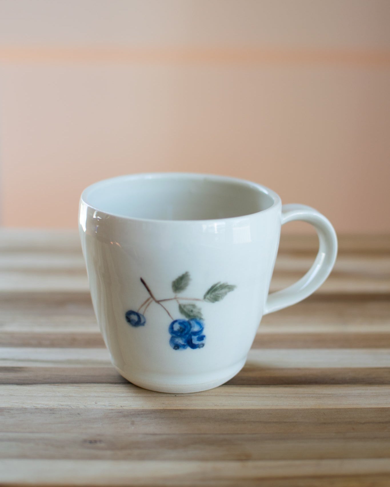 White mug with blueberry design on a wooden surface