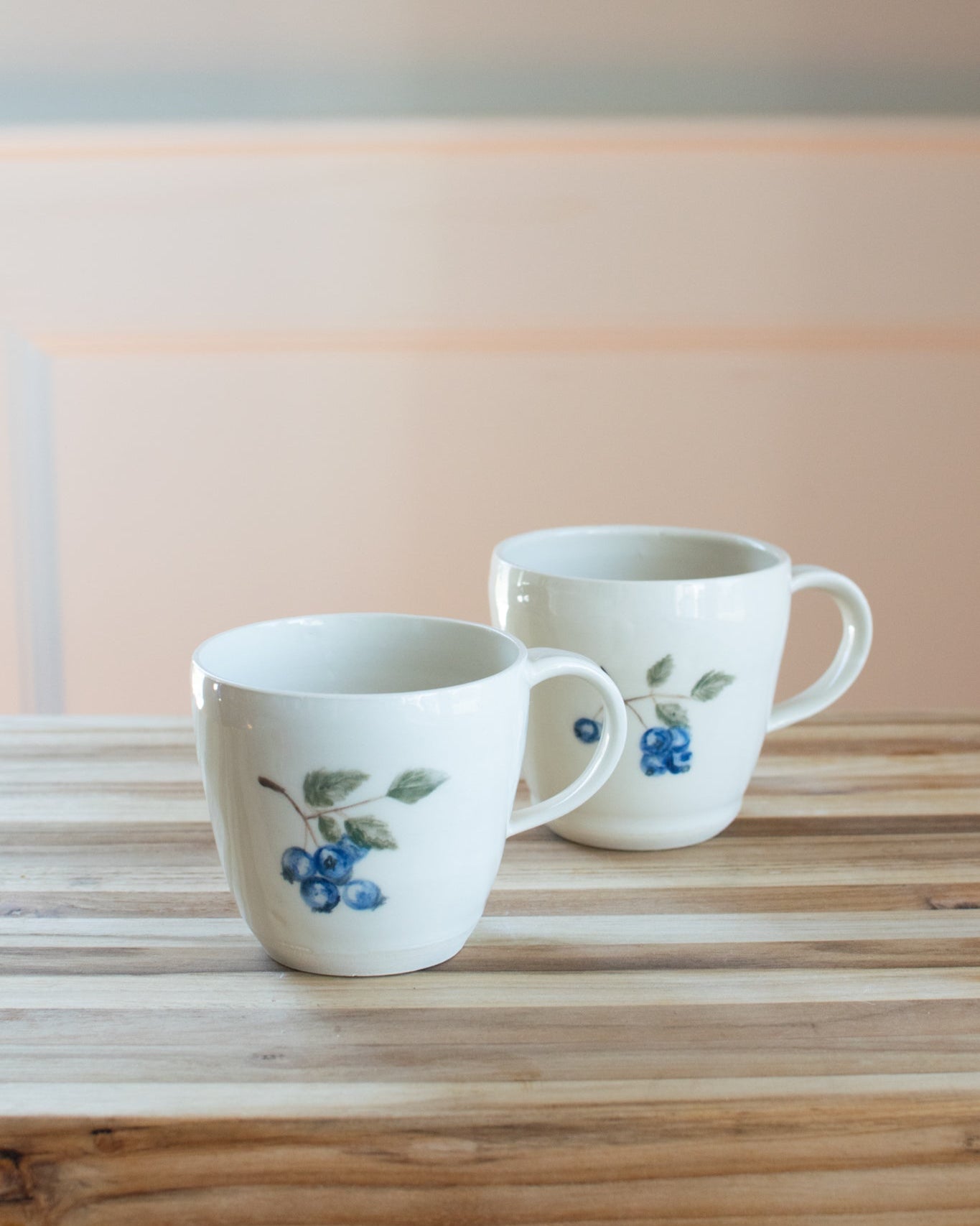 Two white mugs with blueberry design on a wooden surface