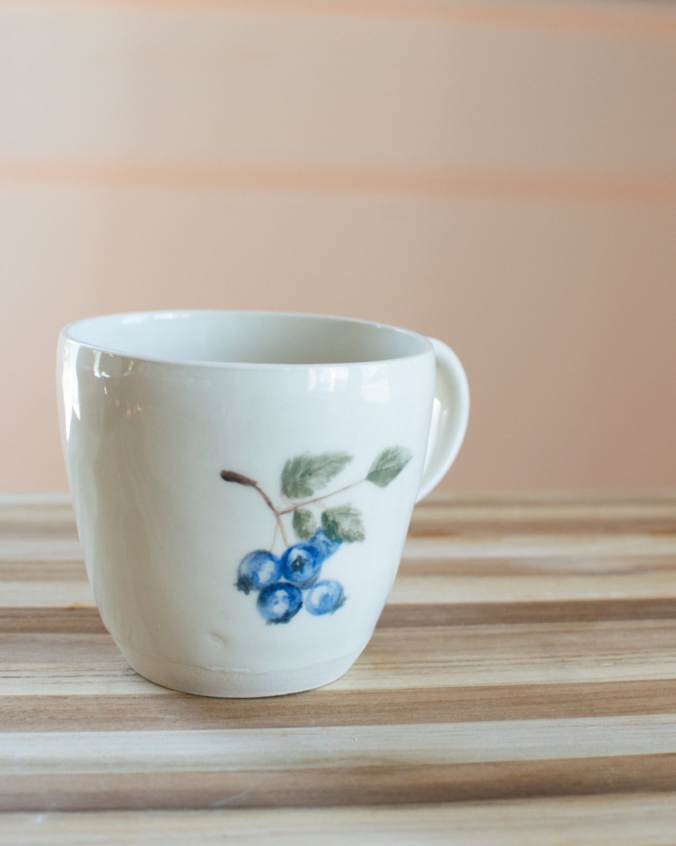 Two white mugs with blueberry design on a wooden surface