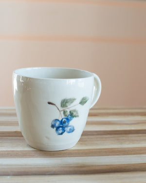 White mug with blueberry design on a wooden surface
