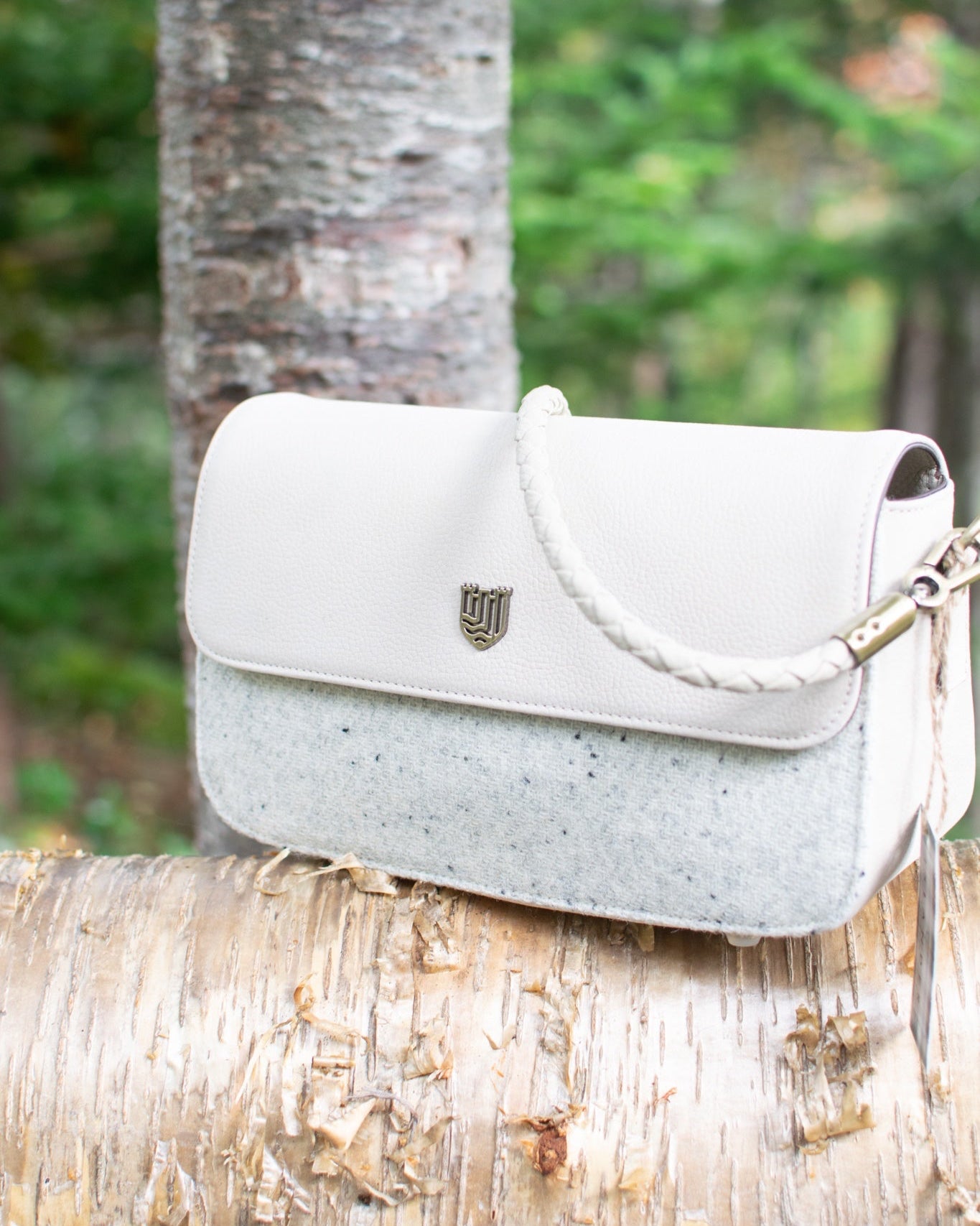 White handbag with a brand logo on a tree branch in a forest setting