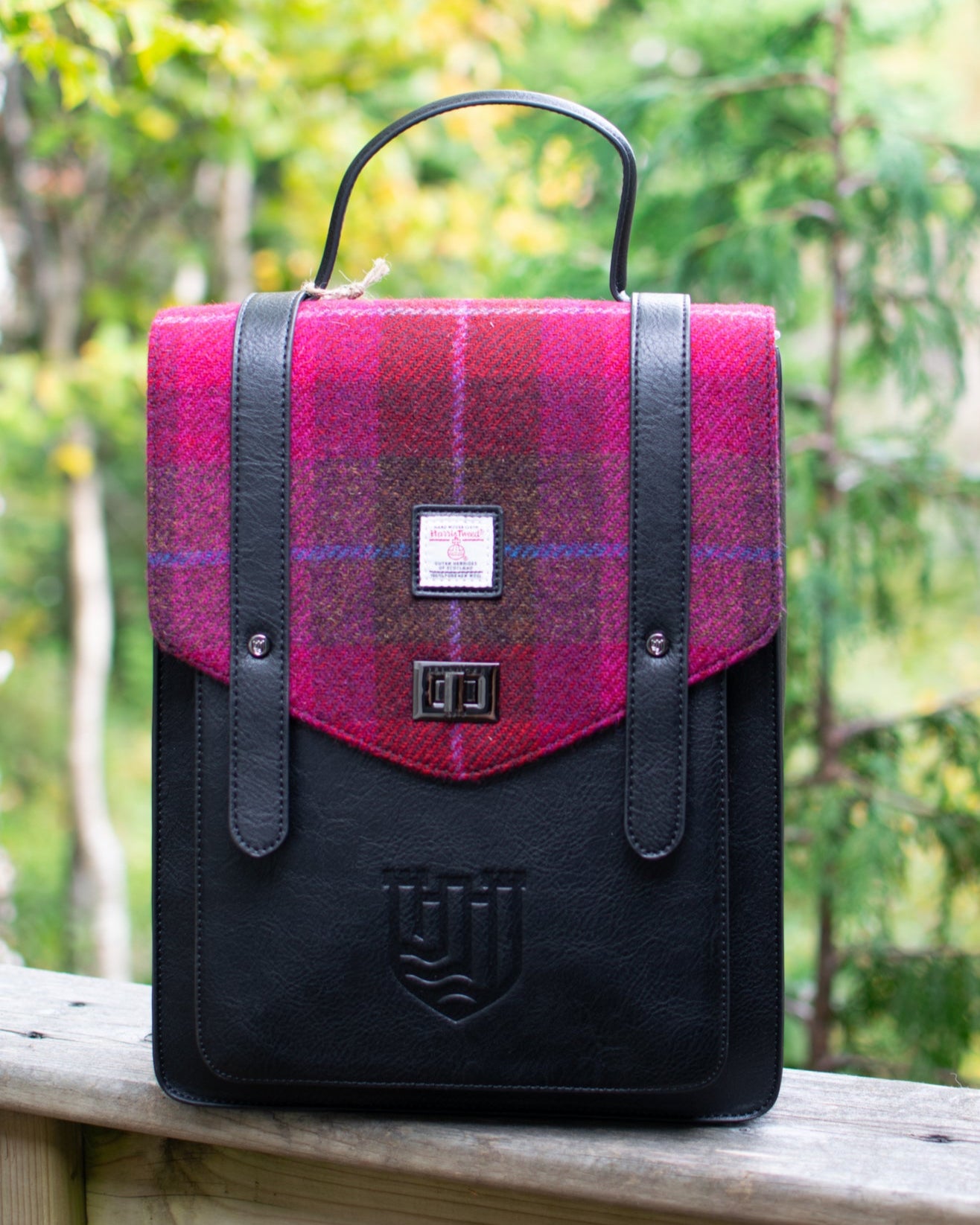 Backpack with pink plaid pattern and black accents on a wooden surface with a blurred natural background