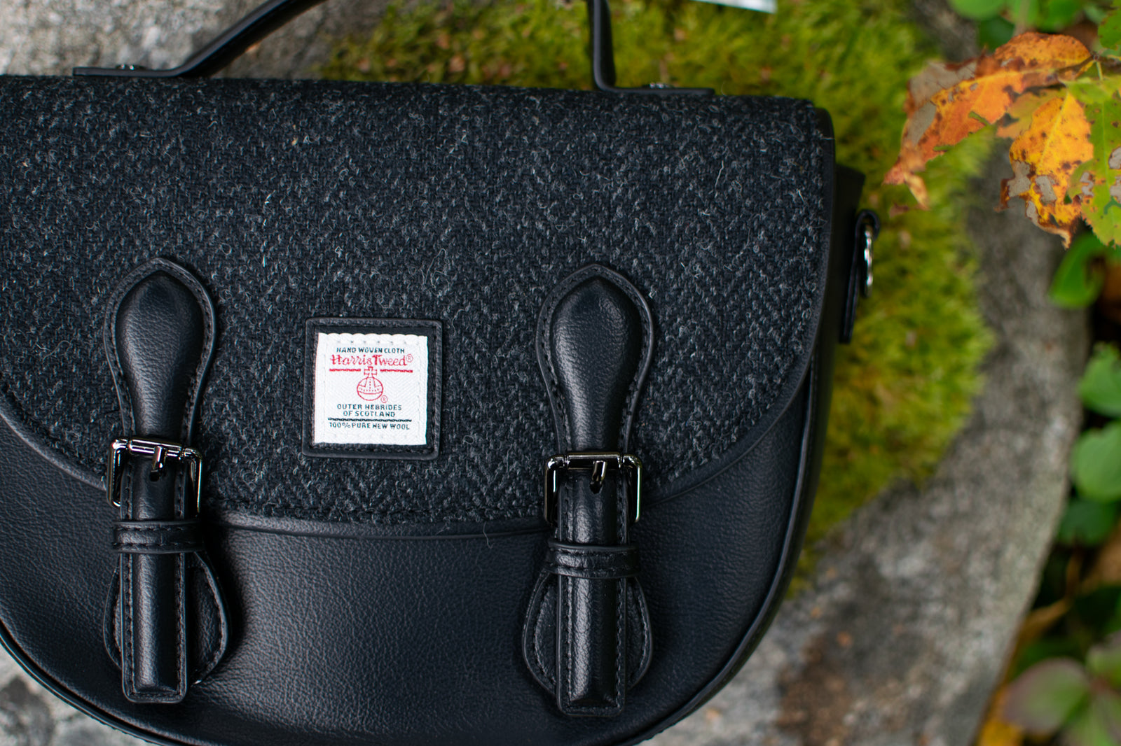 Black textured handbag on a stone surface with green moss and leaves.