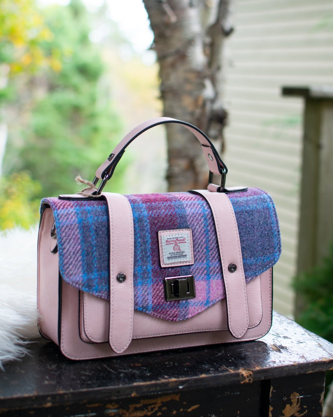 Pink and blue plaid handbag on a wooden surface with a blurred outdoor background