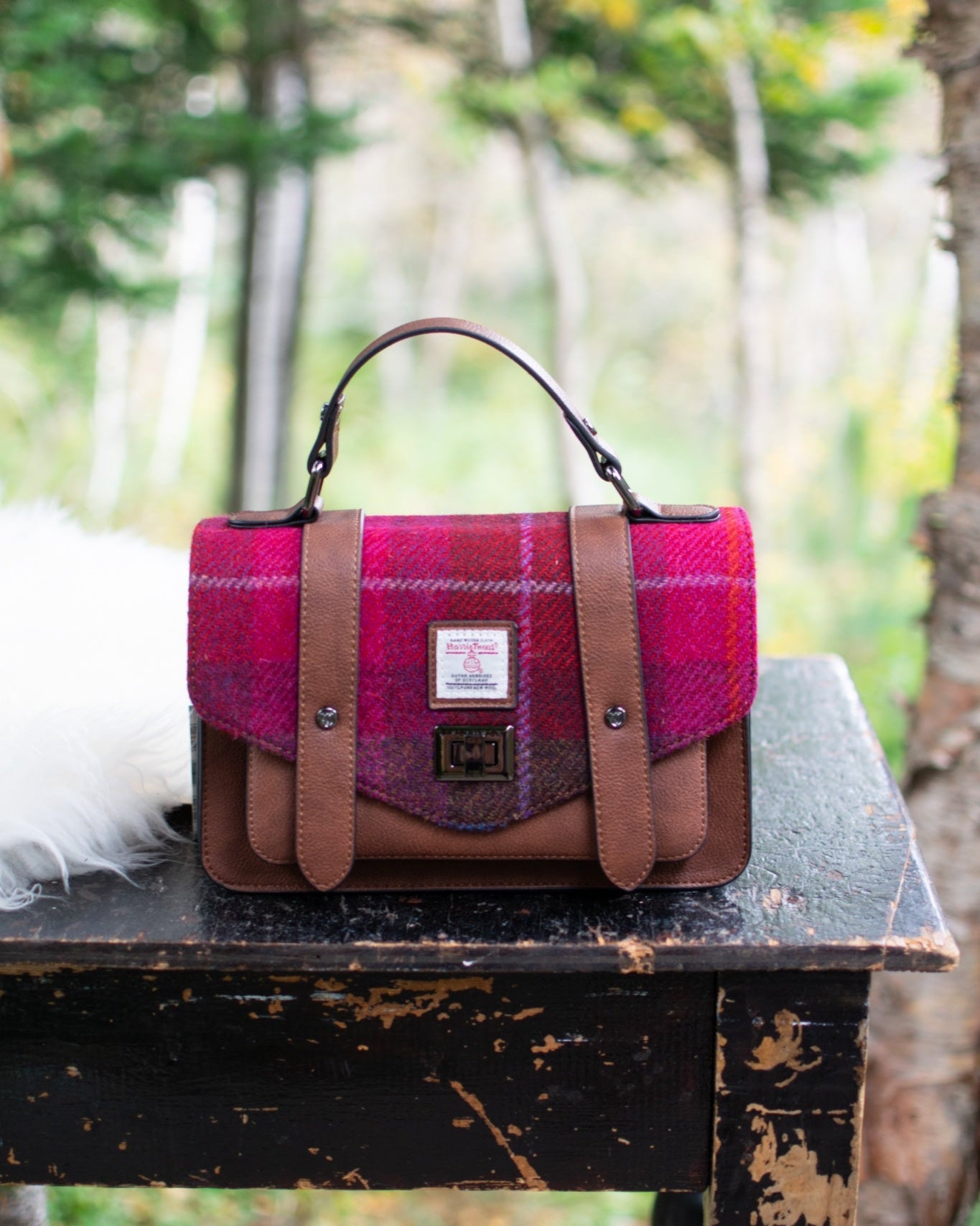 Pink and brown checkered bag on a wooden table with a forest background