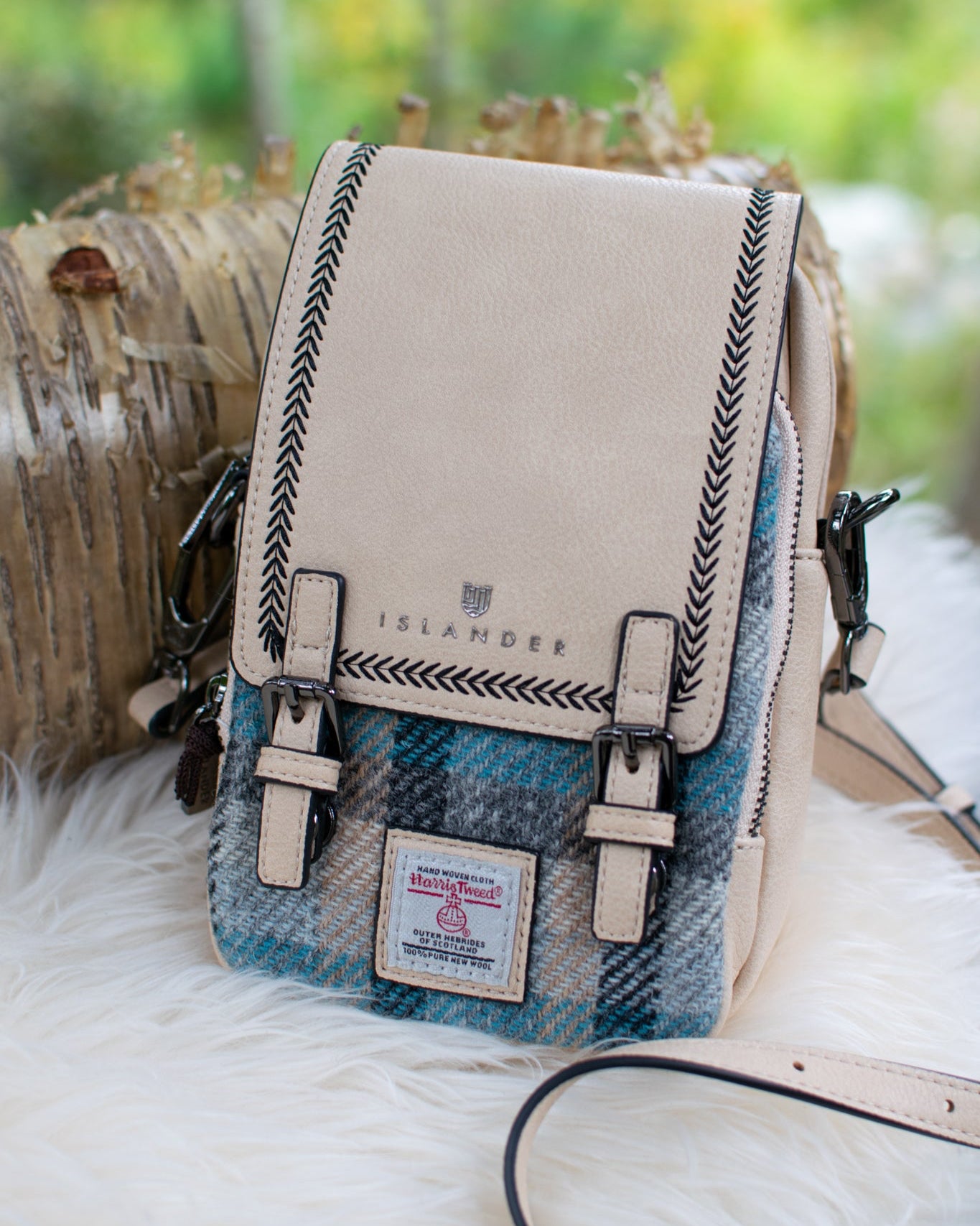 Crossbody bag with plaid pattern and beige top section on a fluffy white surface with blurred natural background