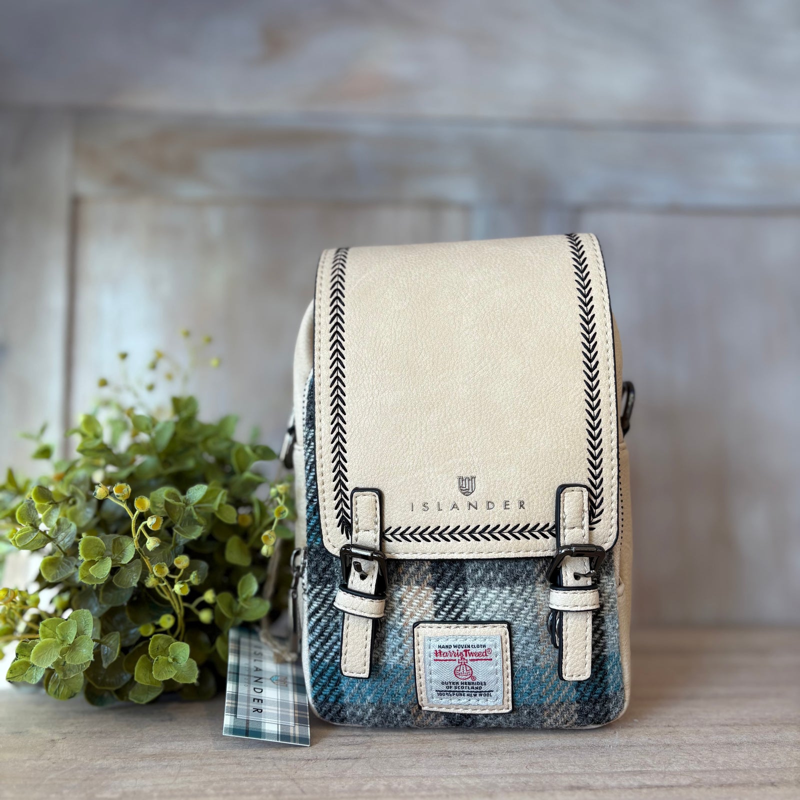 Crossbody bag with plaid pattern and beige top section on a fluffy white surface with blurred natural background